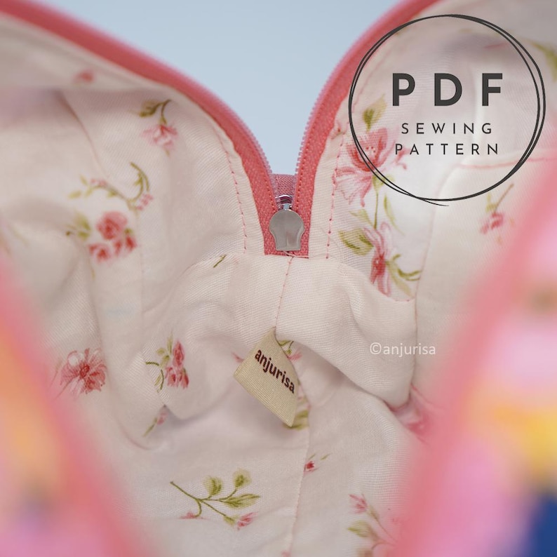 May include: A fabric pouch interior featuring a white lining with a pink floral pattern, a pink zipper closure, and a small beige fabric tag labeled anjurisa. The image includes a circular overlay with the text PDF SEWING PATTERN.