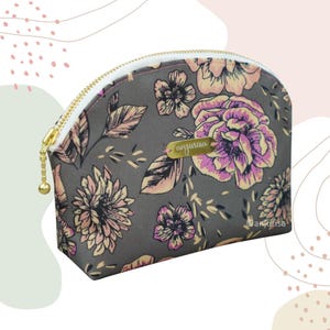 Puede incluir: Una bolsa de maquillaje floral gris con una cremallera dorada y una etiqueta de nombre dorada que dice "anjurisa".