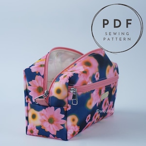 May include: A zippered pouch featuring a dark blue fabric with a pink and yellow floral pattern. The pouch has a pink zipper closure and a secondary front zippered pocket. Text in the upper right corner reads PDF SEWING PATTERN.