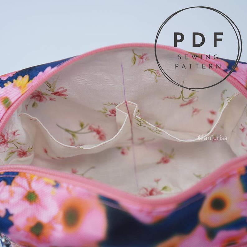 May include: A fabric pouch with a pink zipper and a floral print exterior featuring pink and yellow flowers on a dark blue background. The interior is lined with cream fabric featuring a small pink floral pattern and two open pockets. Text reads PDF SEWING PATTERN.