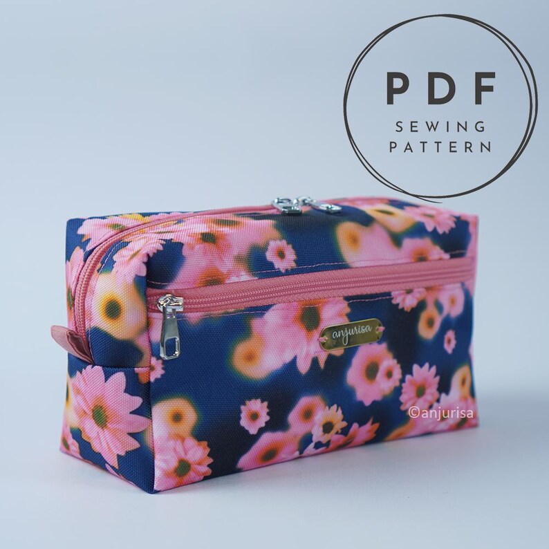 May include: A rectangular zippered pouch featuring a dark blue background with a pink and orange floral pattern. The pouch has a pink zipper, a front zippered pocket, and a small gold-toned metal label with the text anjurisa attached.