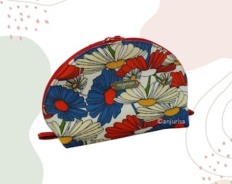 May include: A semi-circular pouch featuring a vibrant floral pattern of red, blue, and cream-colored daisies on a white background. The pouch has a red zipper closure along the top edge and a small metallic tag labeled anjurisa on the front.