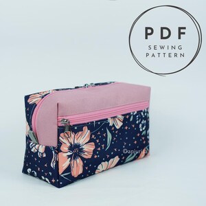 May include: A rectangular zippered pouch featuring a dark blue fabric with a peach-colored floral pattern and a solid pink top panel. The pouch has a pink zipper and a silver metal pull. Text in the upper right corner reads PDF SEWING PATTERN.