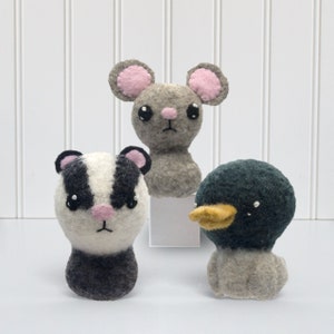 May include: Three felt animal toys: a gray mouse with pink ears and eyes, a black and white badger with a pink nose, and a gray duck with a black head and yellow beak.