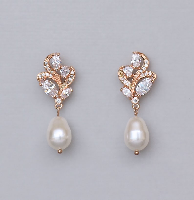 May include: Rose gold earrings with a pearl drop and a cluster of clear cubic zirconia stones in a floral design.