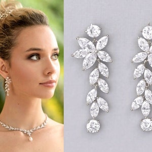 May include: A pair of long, silver dangle earrings with a floral design and clear cubic zirconia stones. The earrings are approximately 3 inches long.