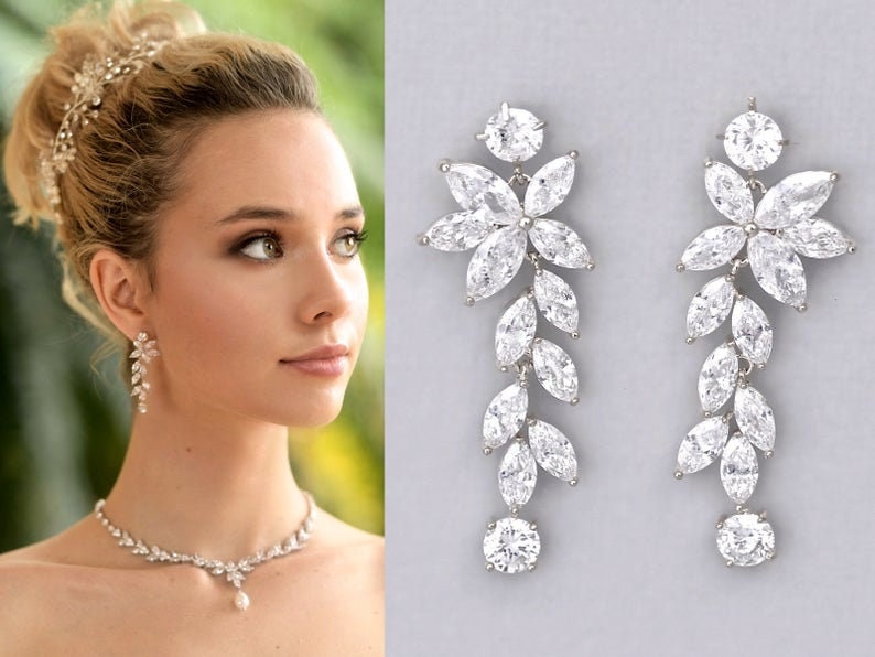 May include: A pair of long, silver dangle earrings with a floral design and clear cubic zirconia stones. The earrings are approximately 3 inches long.