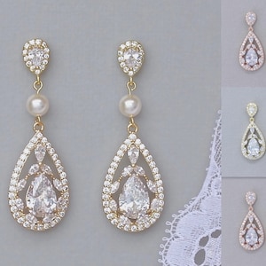 May include: A pair of gold teardrop earrings with a pearl accent and a large crystal in the centre. The earrings are shown in three different metal finishes: gold, silver, and rose gold.