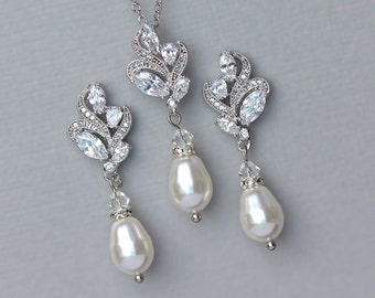 May include: A silver-toned jewelry set featuring a necklace and matching earrings. The necklace has a pendant with a floral design, adorned with clear crystals and a large pear-shaped pearl. The earrings mirror the pendant design, also with pearl drops.