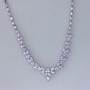 May include: A silver necklace with a delicate design featuring a row of small, clear stones. The stones are arranged in a leaf-like pattern, creating a flowing and elegant look.