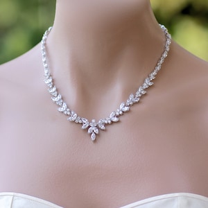 May include: A silver necklace with a delicate design featuring clear cubic zirconia stones. The necklace has a leaf-like pattern and a pendant in the center.