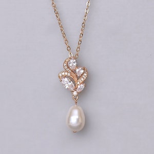 May include: A gold necklace with a delicate pendant featuring a cluster of clear cubic zirconia stones and a single pearl drop.