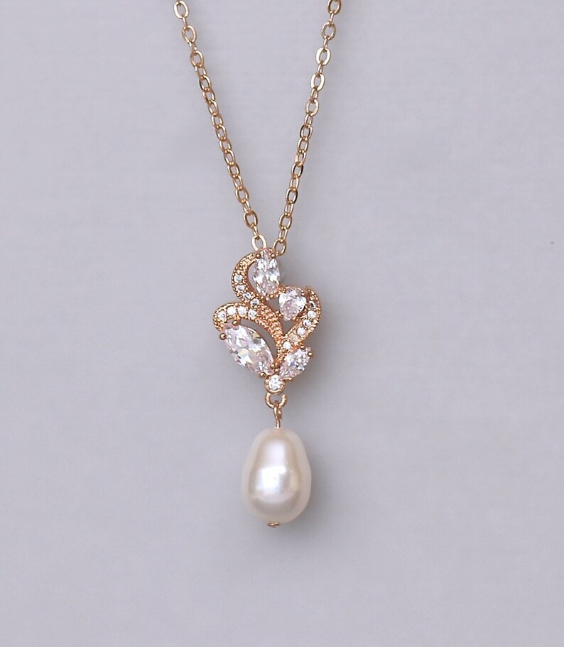 May include: A gold necklace with a delicate pendant featuring a cluster of clear cubic zirconia stones and a single pearl drop.