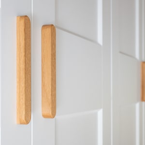 May include: White cabinet doors with wooden handles. The handles are rectangular and have a light wood finish.