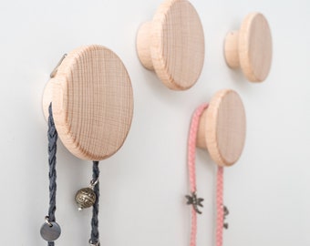 May include: Four round wooden wall hooks with a natural wood finish. Two hooks have grey and pink cords hanging from them.