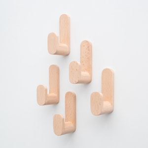 May include: Five light-coloured wooden wall hooks against a white backdrop. Each hook features a rectangular base and a curved hook. The hooks are crafted from natural wood with a smooth finish, suitable for hanging coats, bags, or other items.