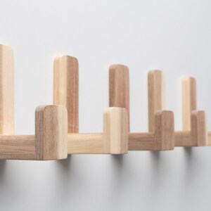 May include: A set of six wooden wall hooks in a light brown color. The hooks are arranged in a row and are all facing the same direction. The hooks are made of solid wood and have a simple, modern design.
