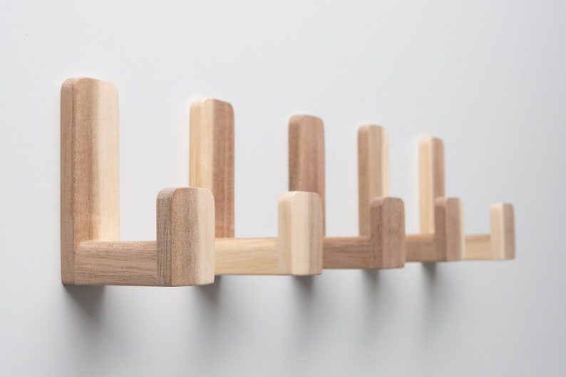 May include: A set of six wooden wall hooks in a light brown color. The hooks are arranged in a row and are all facing the same direction. The hooks are made of solid wood and have a simple, modern design.