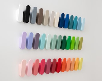 May include: A collection of colorful wall hooks in a variety of shades, including white, black, blue, green, and red. The hooks are arranged in rows, showcasing a spectrum of colors. Each hook has a rounded top and a rectangular base, perfect for hanging items.