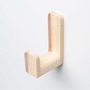 May include: A light brown wooden hook mounted on a white wall. The hook is shaped like a letter J and has a rounded end.