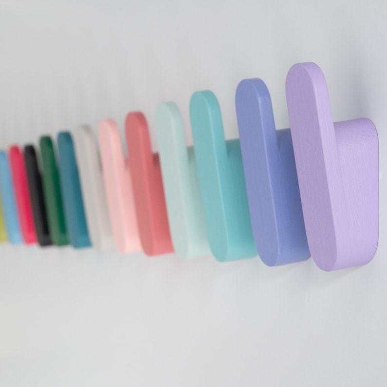 May include: A series of pastel-coloured wooden wall hooks, mounted on a white wall. The hooks are in shades of pink, blue, and green, offering a decorative and practical storage option. Each hook features a rounded, curved design.