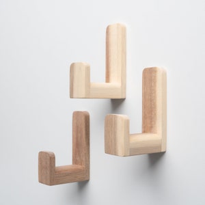 May include: Three wooden wall hooks in the shape of the letter J. The hooks are light brown and are mounted on a white wall.