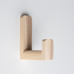 May include: A wooden wall hook with a simple, L-shaped design. The hook is made of light-colored wood and has a smooth finish.