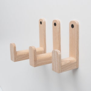 May include: Three wooden wall hooks with a rounded, curved design. The hooks are made of light wood and are mounted on a white wall.