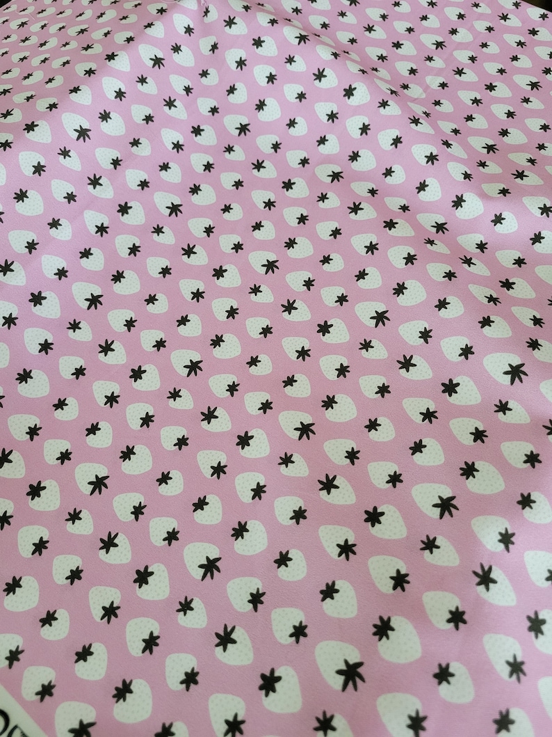 May include: Pink fabric with a repeating pattern of white strawberries and black five-pointed stars.