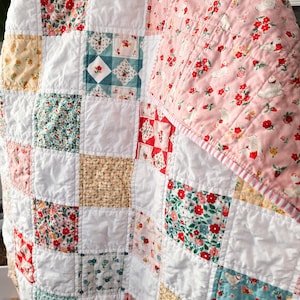May include: A patchwork quilt with a variety of floral and patterned fabrics in red, pink, blue, and yellow squares, interspersed with white squares. The quilt has a pink floral patterned backing with white swans.