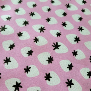 May include: Pink fabric with a repeating pattern of white strawberries and black five-pointed stars.