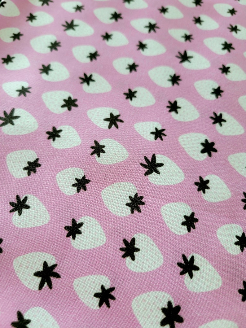 May include: Pink fabric with a repeating pattern of white strawberries and black five-pointed stars.