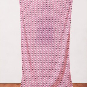 May include: A pink fabric with a white and black strawberry pattern. The fabric is being held up by a person's hands.