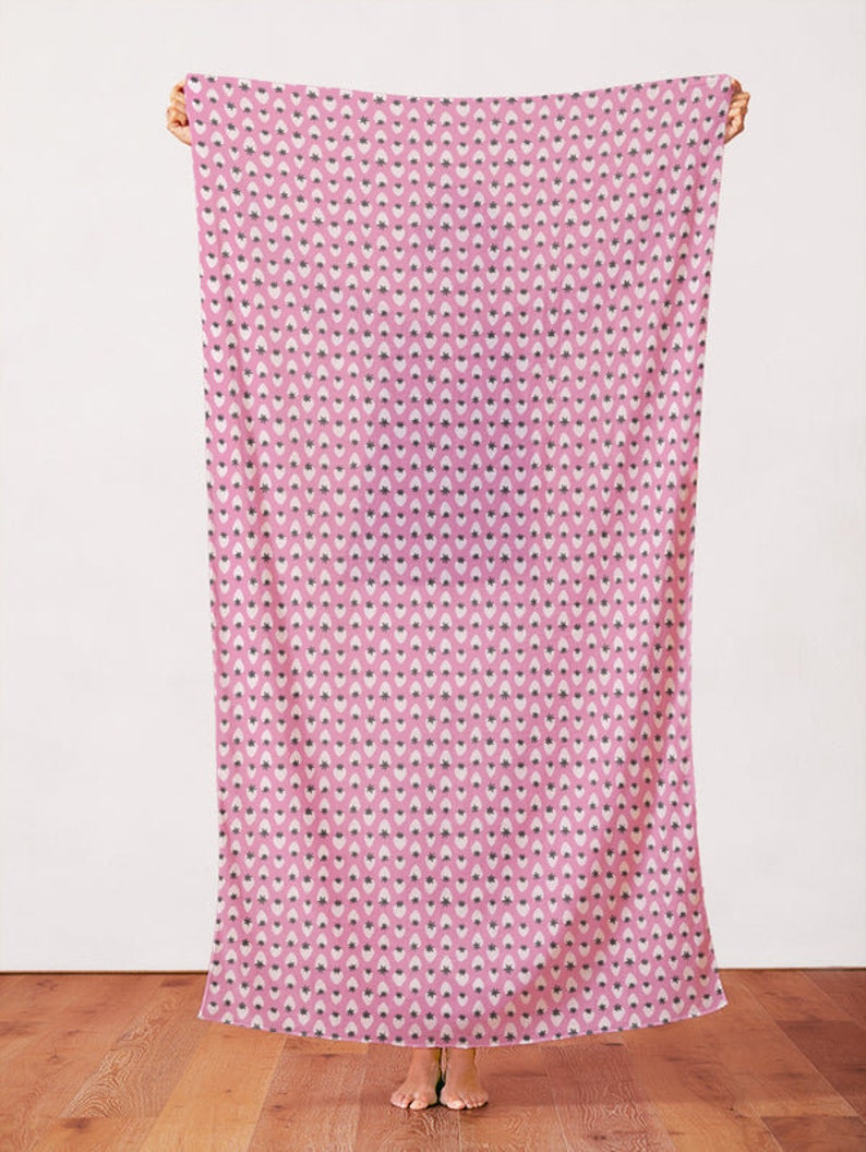 May include: A pink fabric with a white and black strawberry pattern. The fabric is being held up by a person's hands.