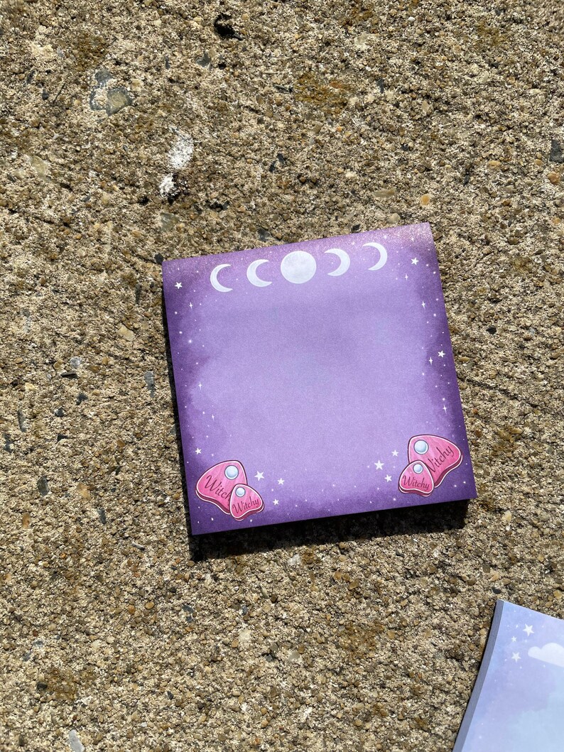 A purple sticky note with a moon and star motif is lying on a concrete surface.