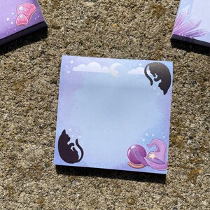a square notepad with a purple background and illustrations of cats and a crystal ball.