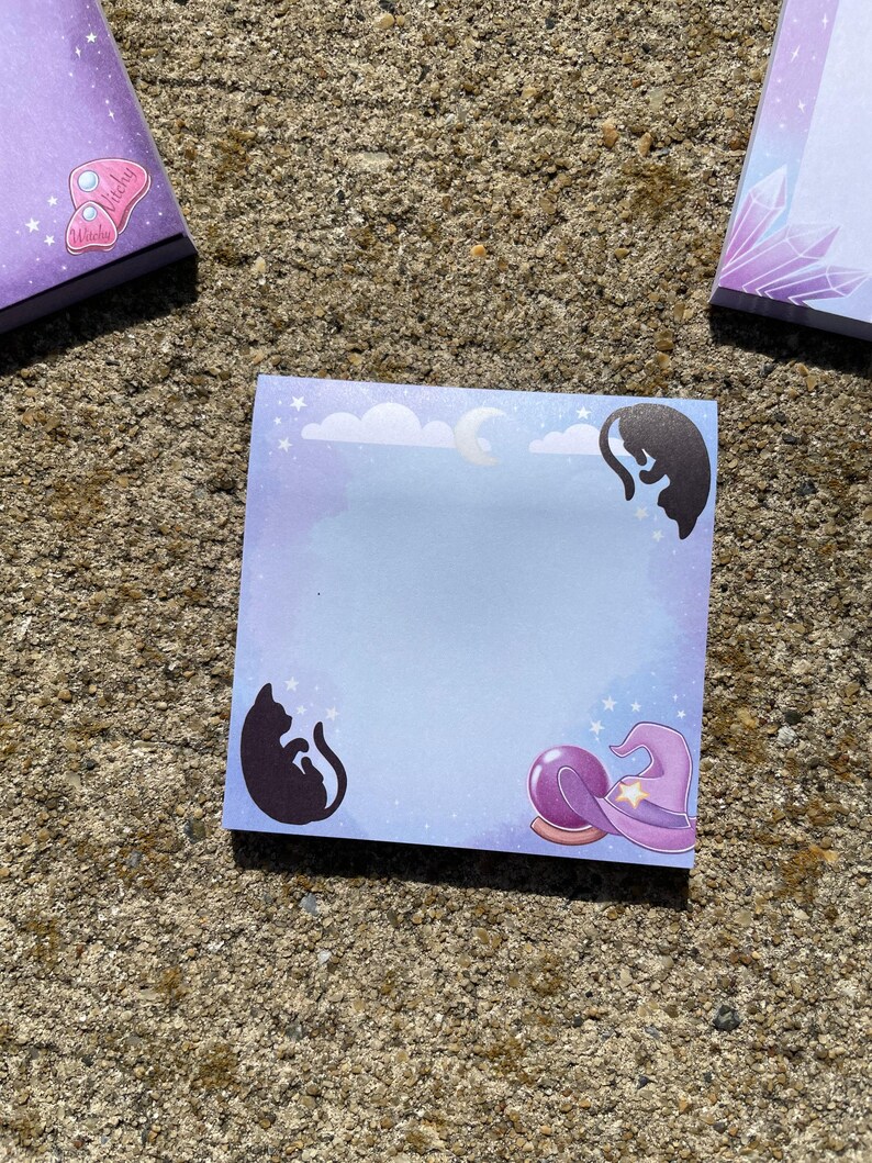 a square notepad with a purple background and illustrations of cats and a crystal ball.