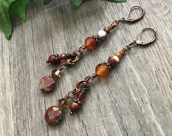 May include: A pair of long dangle earrings featuring copper-toned wire and hardware with faceted brown and orange gemstone beads, smooth round earth-toned stone beads, and small clear crystal accents, finished with secure lever-back closures.
