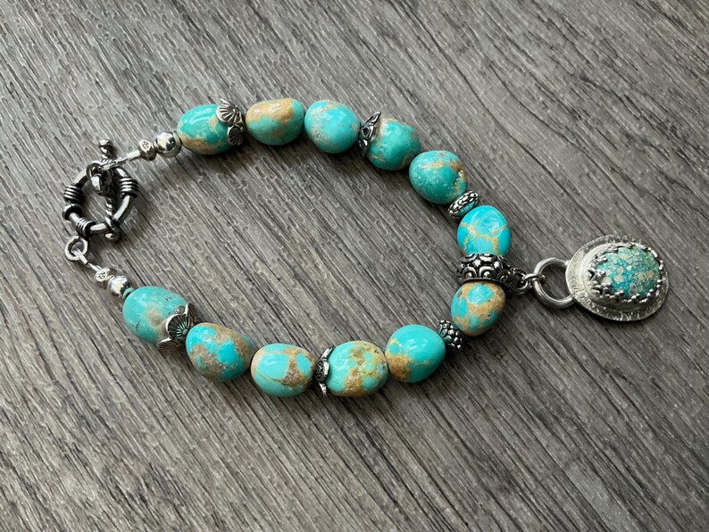 May include: A bracelet featuring polished turquoise beads with brown matrix patterns, interspersed with small silver-toned metal spacers and decorative beads. The piece includes a toggle clasp and a single oval pendant with a bezel-set turquoise stone.