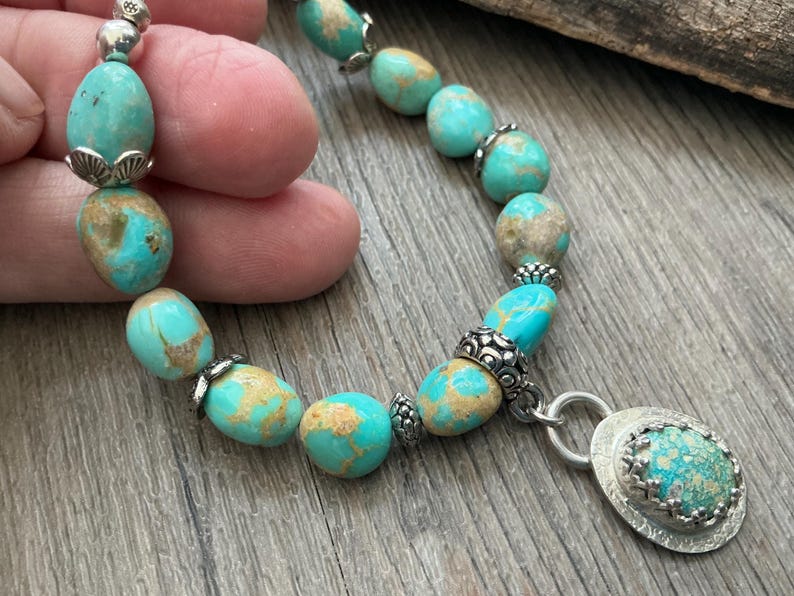 May include: A bracelet featuring polished, oval-shaped turquoise beads with brown matrix veining, interspersed with ornate silver-toned metal spacers and bead caps, finished with a circular silver-toned pendant containing a matching turquoise stone.