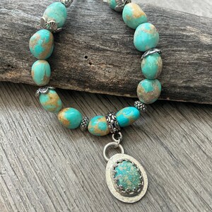 May include: A bracelet featuring smooth, rounded turquoise beads with brown matrix patterns, interspersed with small, decorative silver-toned metal spacers. A central oval pendant with a matching turquoise stone set in a textured silver-toned bezel.