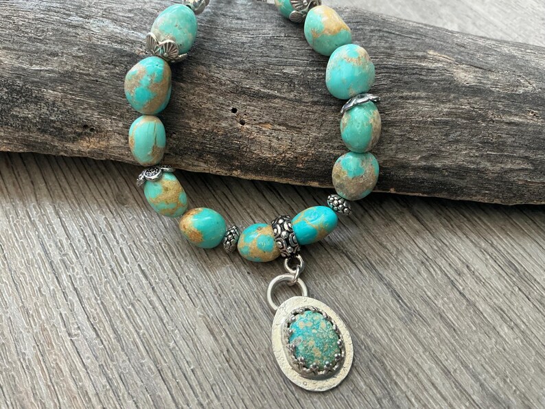 May include: A bracelet featuring smooth, rounded turquoise beads with brown matrix patterns, interspersed with small, decorative silver-toned metal spacers. A central oval pendant with a matching turquoise stone set in a textured silver-toned bezel.