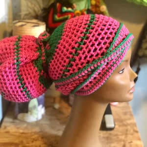 May include: A pink and green crocheted hat with a bun cover. The hat is made with a simple stitch pattern and has a wide brim. The bun cover is attached to the back of the hat and is also crocheted.