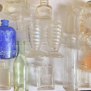 May include: A collection of antique glass bottles and jars in various shapes and sizes. Includes a cobalt blue bottle, clear bottles with embossed designs, and an amber-colored jar. Some bottles have visible text.
