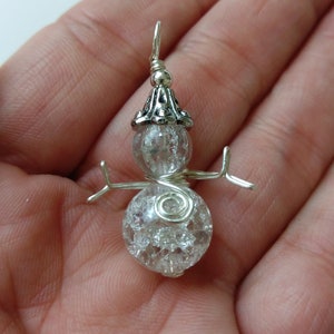 May include: A silver wire snowman charm with a clear glass bead head and body. The snowman has a silver bead hat with a decorative design.