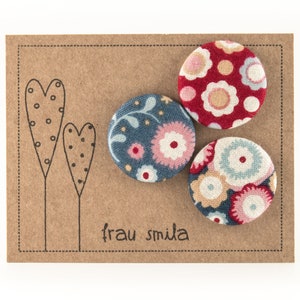 Puede incluir: Tres botones cubiertos de tela con patrones florales. Los botones est&aacute;n en una tarjeta marr&oacute;n con el texto "frau smida" impreso en ella.