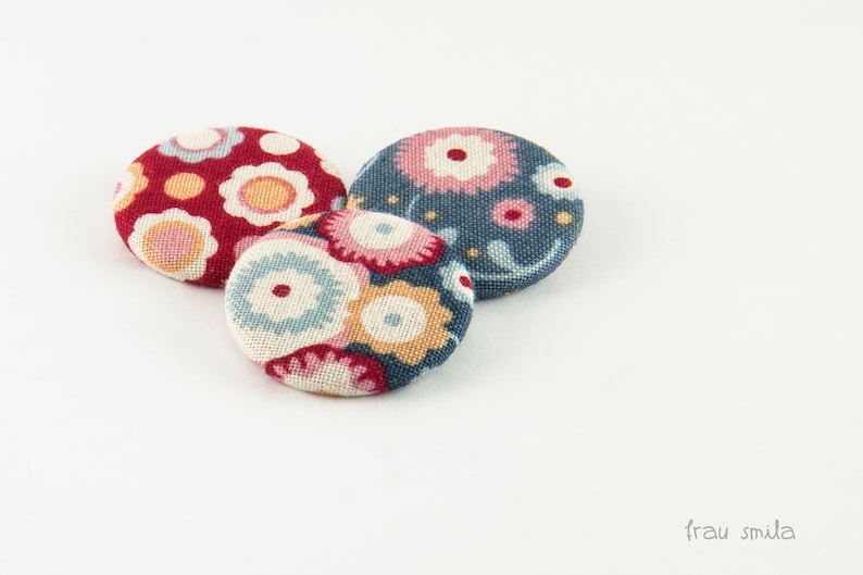 Puede incluir: Tres botones cubiertos de tela con motivos florales. Los botones son rojos, azules y blancos con una variedad de dise&ntilde;os florales.