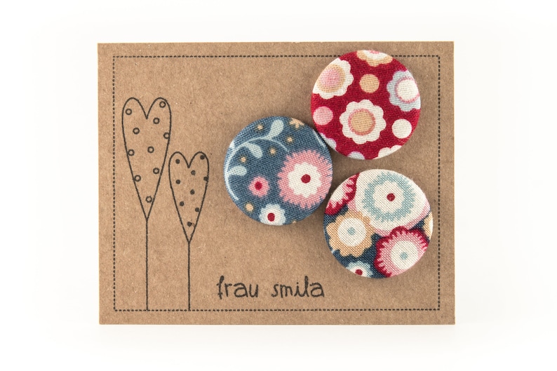 Puede incluir: Tres botones cubiertos de tela con patrones florales. Los botones est&aacute;n en una tarjeta marr&oacute;n con el texto "frau smida" impreso en ella.