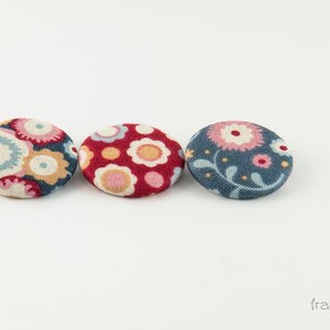Puede incluir: Tres botones cubiertos de tela con motivos florales. Los botones son en tonos de azul, rojo y rosa.