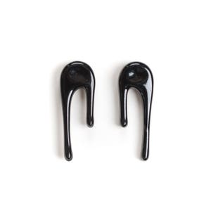 Puede incluir: Un par de pendientes negros abstractos en forma de gota. Los pendientes est&aacute;n hechos de un material liso y brillante.